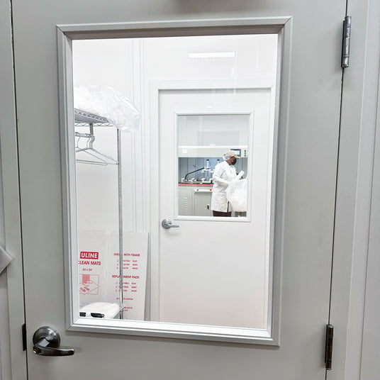 Cleenroom laboratory door with a window, showing a person in a lab coat inside.