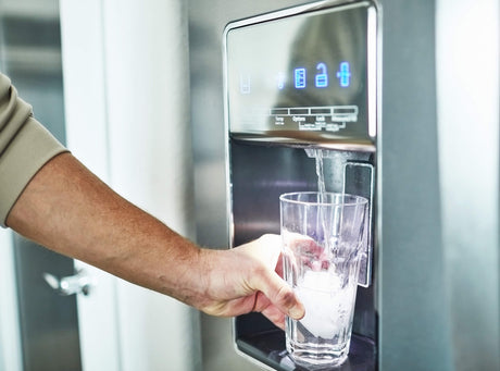 Man's arm filling a glass of water from the fridge dispenser