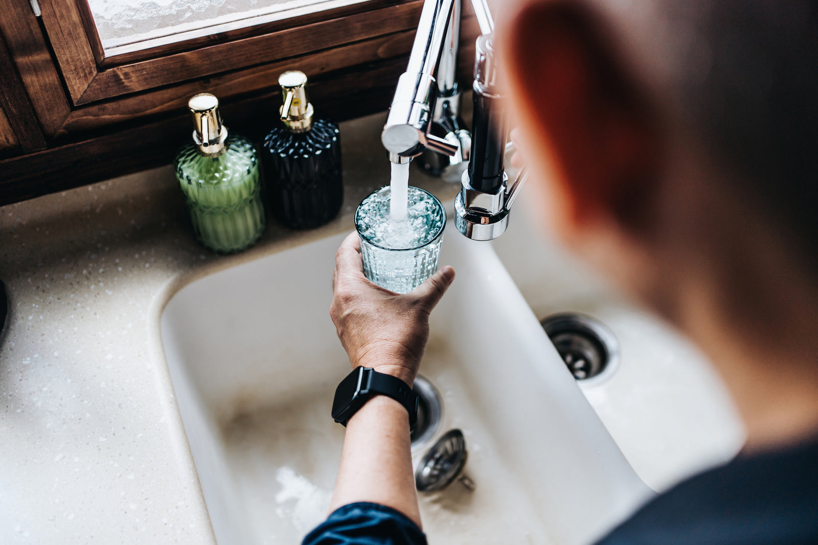 Man filling a glass of water at a sink 