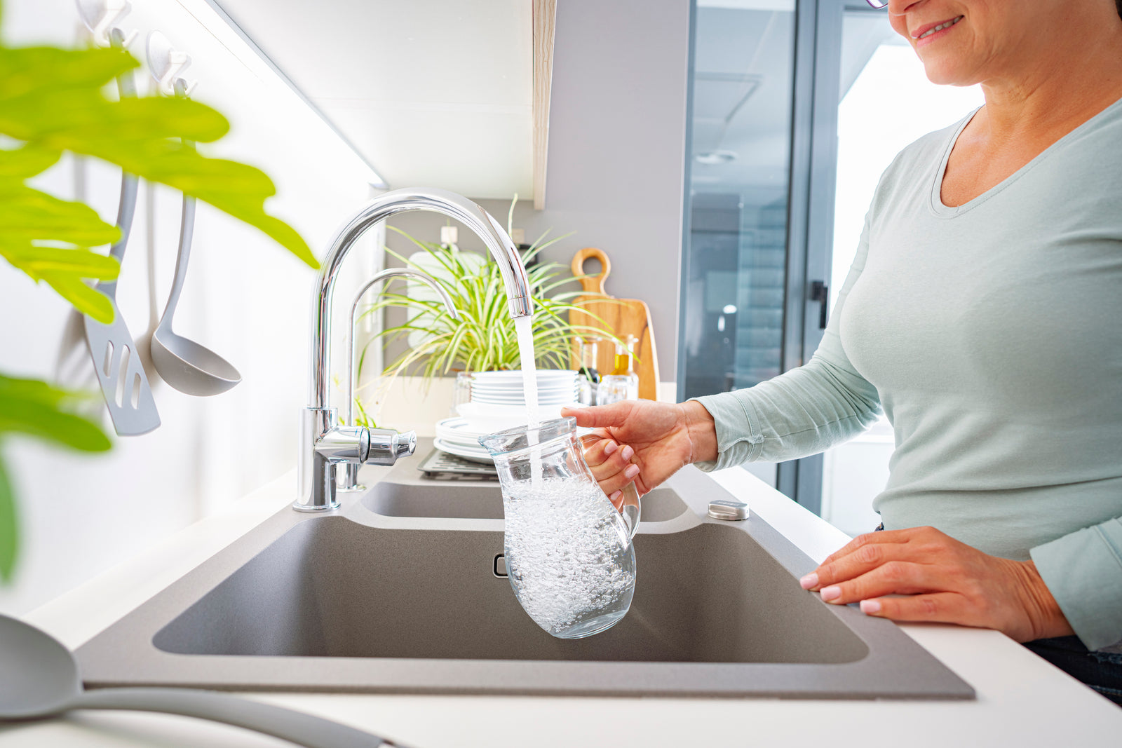 woman filling a water pitcher with tap water at the sink
