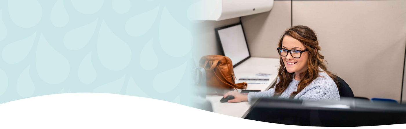 Woman sitting at a desk with a computer, smiling, in an office setting.